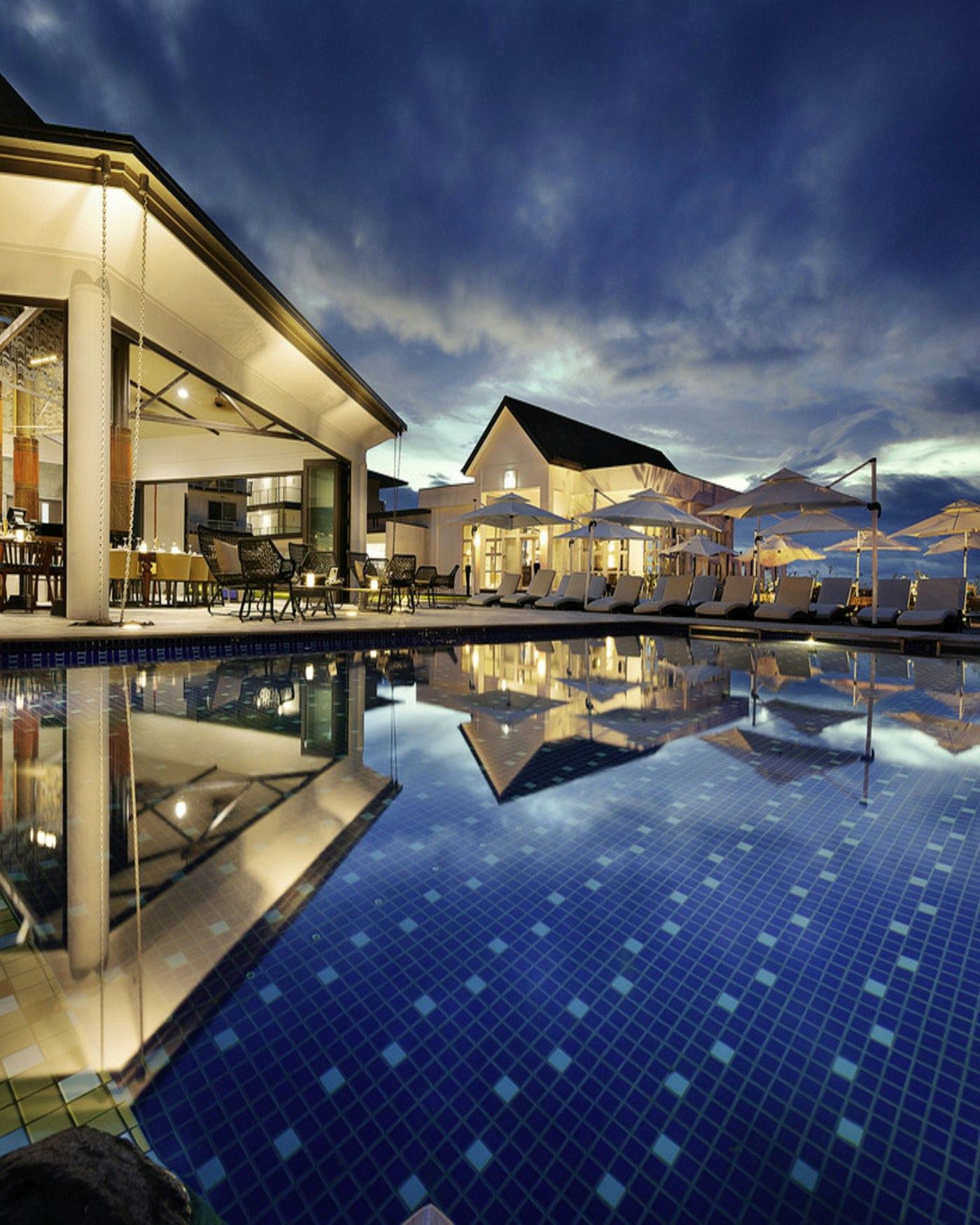 A still resort pool at dusk with palms around the edge